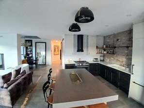 Une cuisine moderne dotée d’un îlot central, de luminaires suspendus noirs et d’un mur d’accent en briques.