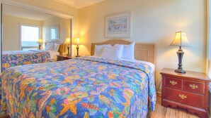 Habitación de hotel con dos camas, un aparador, un espejo y un cuadro en la pared.