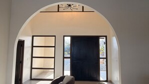 Un intérieur avec une porte en arc de cercle, un canapé, un fauteuil et une grande fenêtre.