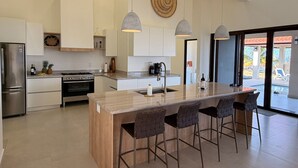 Une cuisine moderne dotée d’un îlot central, d’appareils électroménagers en acier inoxydable et de luminaires suspendus.