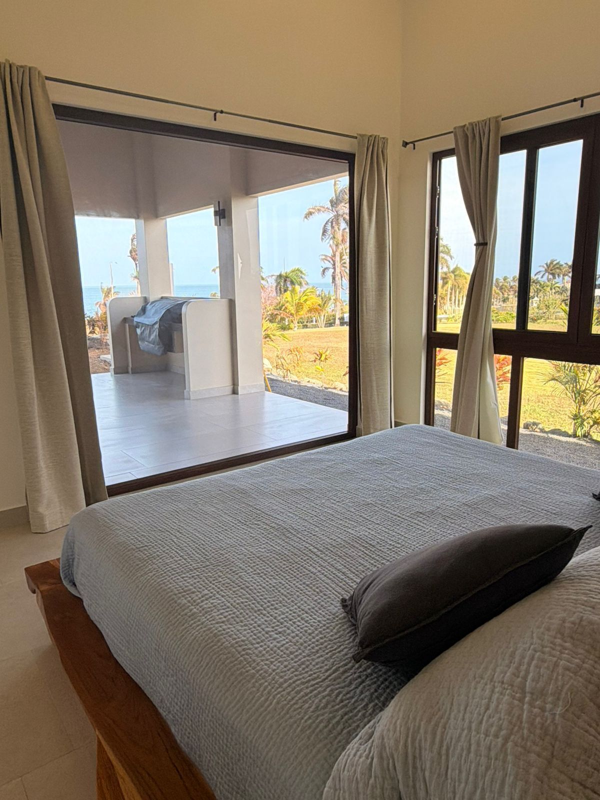 A bedroom with a large bed, a view of a balcony, and a glimpse of the ocean.