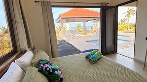 Une chambre avec un lit, une vue sur une piscine et un belvédère, ainsi qu’une grande fenêtre.