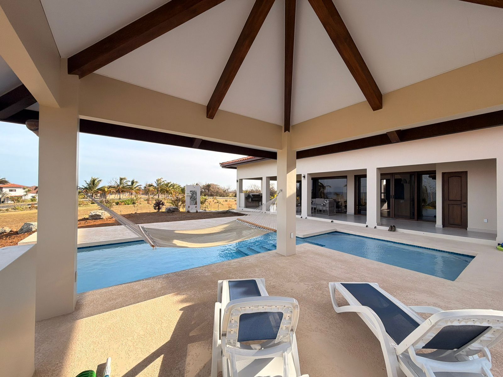 A covered pool area with two lounge chairs, a hammock, and a view of a residential neighborhood.