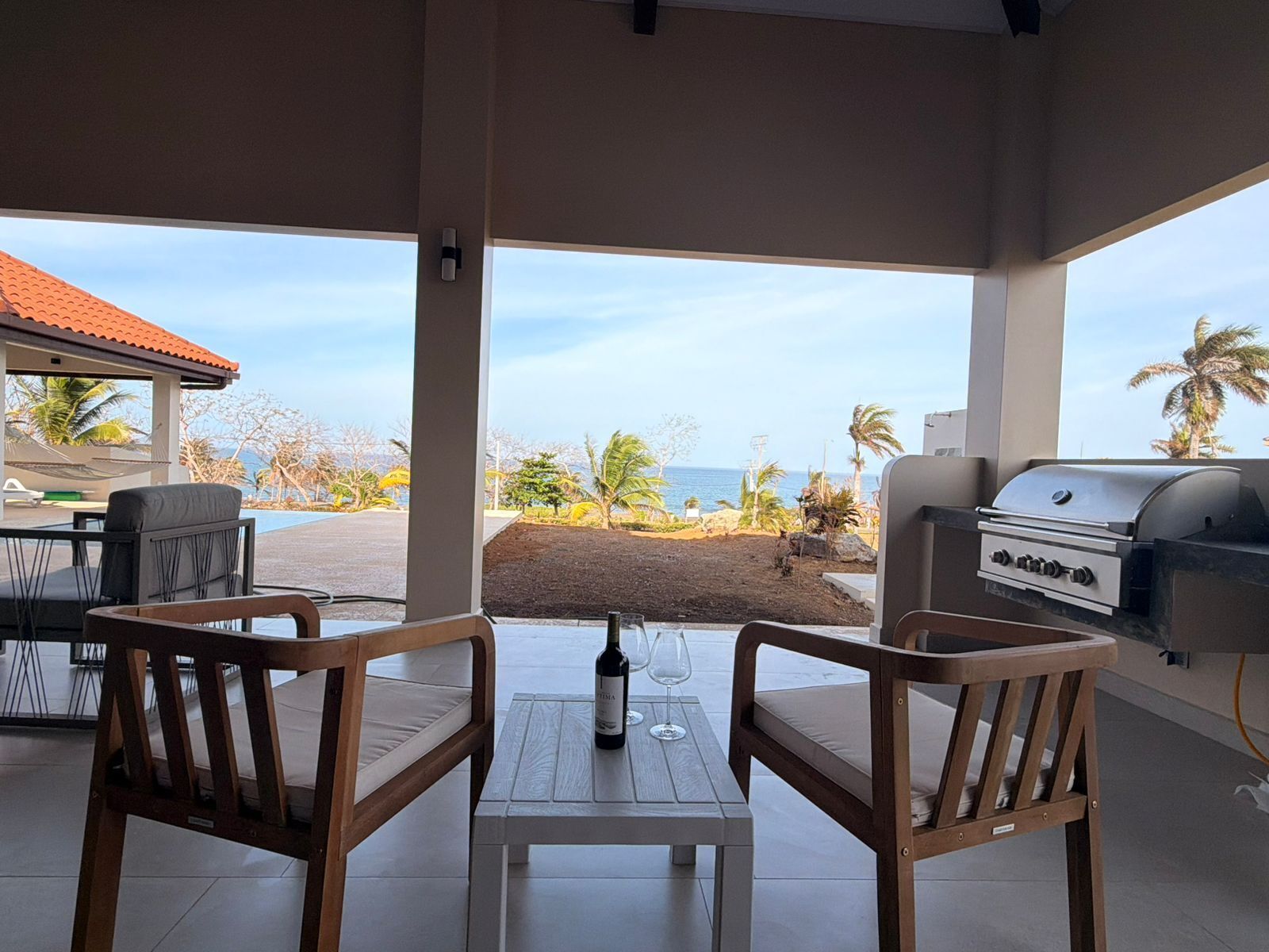 An outdoor seating area with a table, chairs, a grill, and a view of the beach.