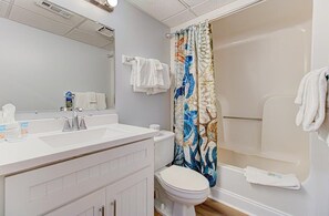Ein Badezimmer mit einem weißen Waschbecken, einer Toilette, einer Dusche mit bunter Duschvorhang und einem Spiegel.