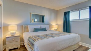 Quarto com cama, duas mesas de cabeceira, espelho e janela com cortinas.