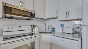 A kitchen with white cabinets, a microwave, an oven, a dishwasher, and a coffee maker. - Oceanfront charm awaits at 0709 Seaside Serenade in Carolina Beach! (Carolina Beach)