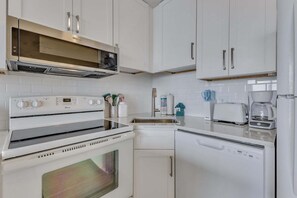Eine Küche mit weißen Schränken, einer Mikrowelle, einem Backofen, einem Geschirrspüler und einer Kaffeemaschine.