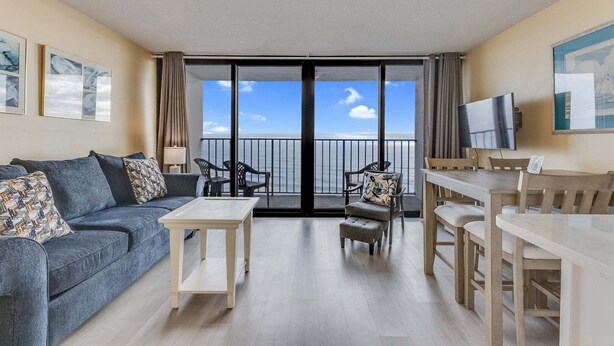 A balcony with a view of the sea, a sofa, a table, and chairs. - Oceanfront charm awaits at 0709 Seaside Serenade in Carolina Beach! (Carolina Beach)