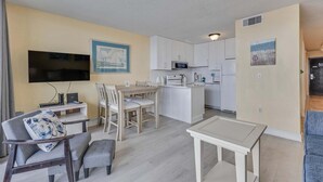 A compact living space with a dining area, kitchenette, and a TV mounted on the wall. - Oceanfront charm awaits at 0709 Seaside Serenade in Carolina Beach! (Carolina Beach)