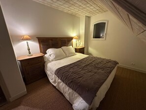 Een slaapkamer met een bed, twee nachtkastjes met lampen, een houten hoofdbord, een klein raam en een vloerbedekking.