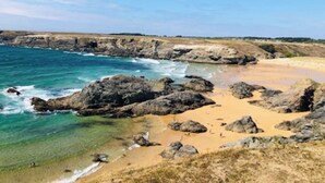 Paisatge costaner amb roques, aigua turquesa i platja sorrenca.