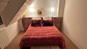 Habitació amb un llit, dos coixins, un capçal, una làmpada de nit, una maleta i una finestra amb vistes.