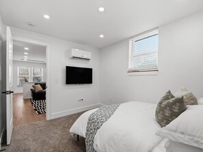 Un dormitorio con cama, televisor montado en la pared, aire acondicionado y ventana con persianas.