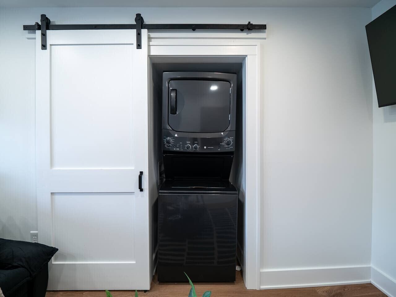 A compact room with a sliding door leading to a laundry area, a small window, and a flat-screen TV mounted on the wall.