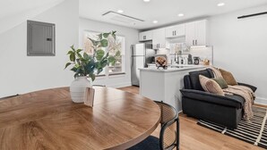 Una cocina moderna con armarios blancos, una isla central y un comedor con una mesa redonda de madera.