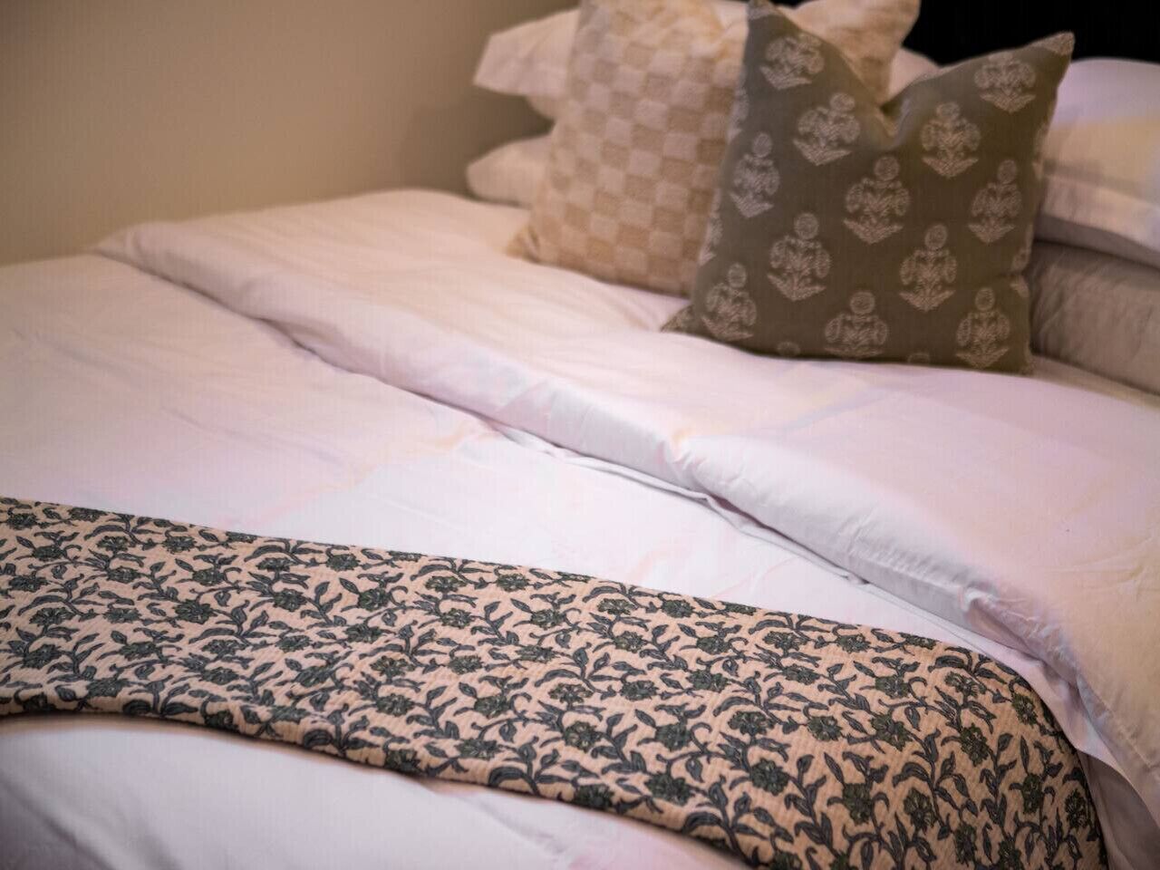 A bed with a patterned bedspread, pillows with a checkered pattern, and a plain white pillow.