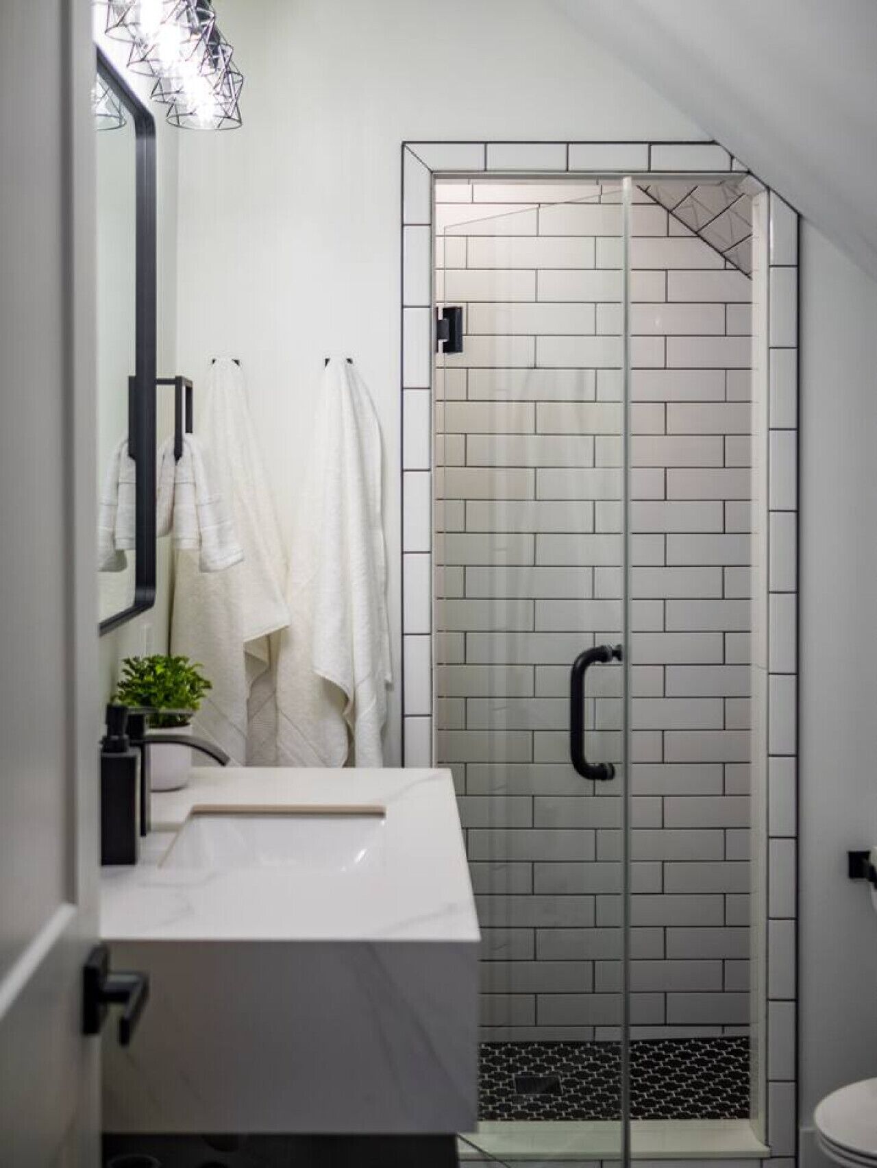 A modern bathroom with a white tiled shower, a sink, and a mirror.