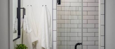 A modern bathroom with a white tiled shower, a sink, and a mirror.