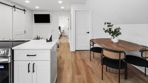 Una cocina moderna con armarios blancos, horno empotrado y comedor con mesa y sillas de madera.