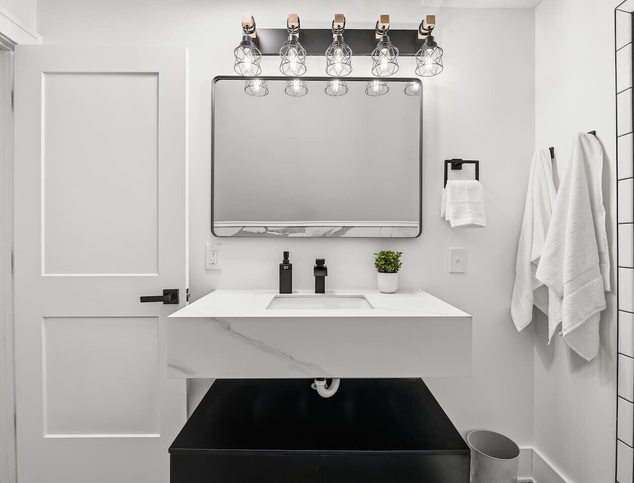 A modern bathroom with a white vanity, black sink, and a large mirror above the sink.