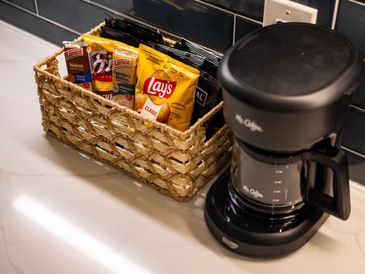 A kitchen counter with a coffee maker and a basket containing snacks.
