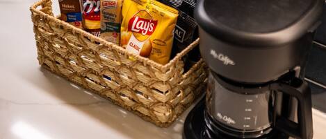 A kitchen counter with a coffee maker and a basket containing snacks.