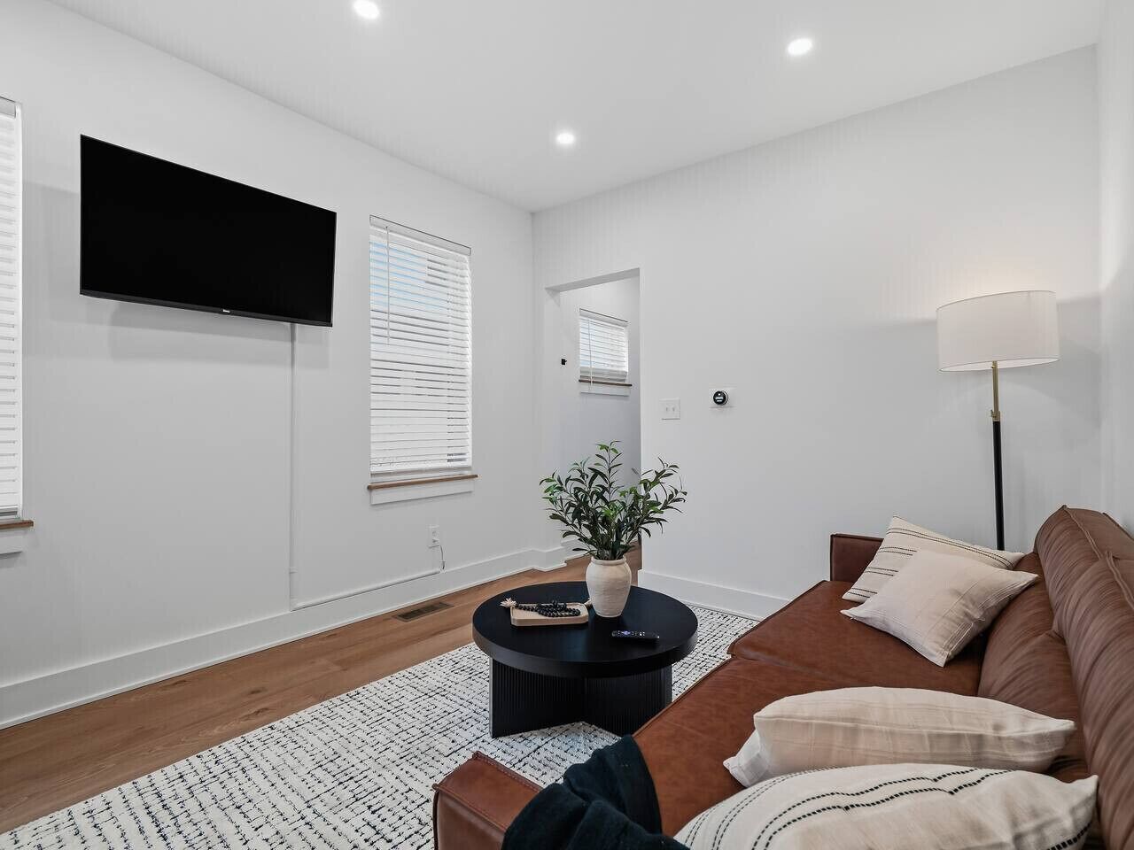A modern living room with a flat-screen TV, a round coffee table, a brown sofa, and a floor lamp.