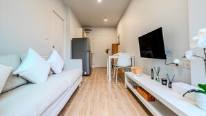 A modern, compact living space with a sofa, TV, and a small dining area. - ZcapeX2 (Choeng Thale)