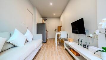 Un espace de vie moderne et compact, comprenant un canapé, un téléviseur et un petit coin repas.
