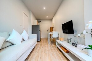 Ein modernes, kompaktes Wohnzimmer mit Sofa, Fernseher und einer kleinen Essecke.