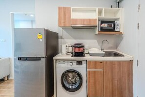 Eine kompakte Küche mit Kühlschrank, Waschmaschine, Mikrowelle und Kaffeemaschine.
