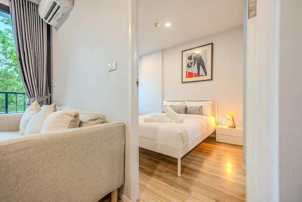 Ein modernes Schlafzimmer mit einer Couch, einem Bett, einem Nachttisch und einer Wand-Klimaanlage.