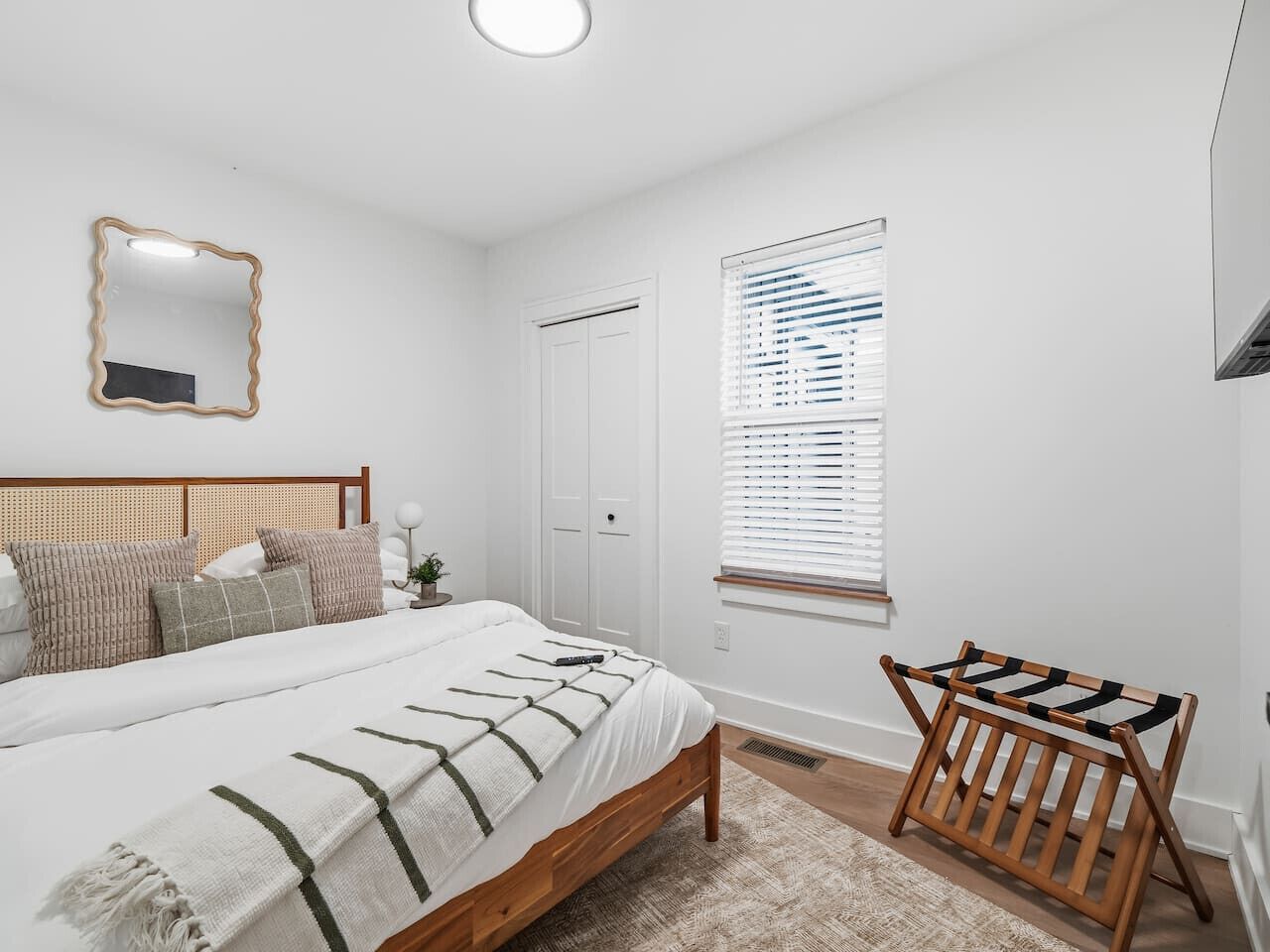 Ein Schlafzimmer mit Bett, Nachttisch, Fenster mit Jalousien und einer hölzernen Sitzbank.