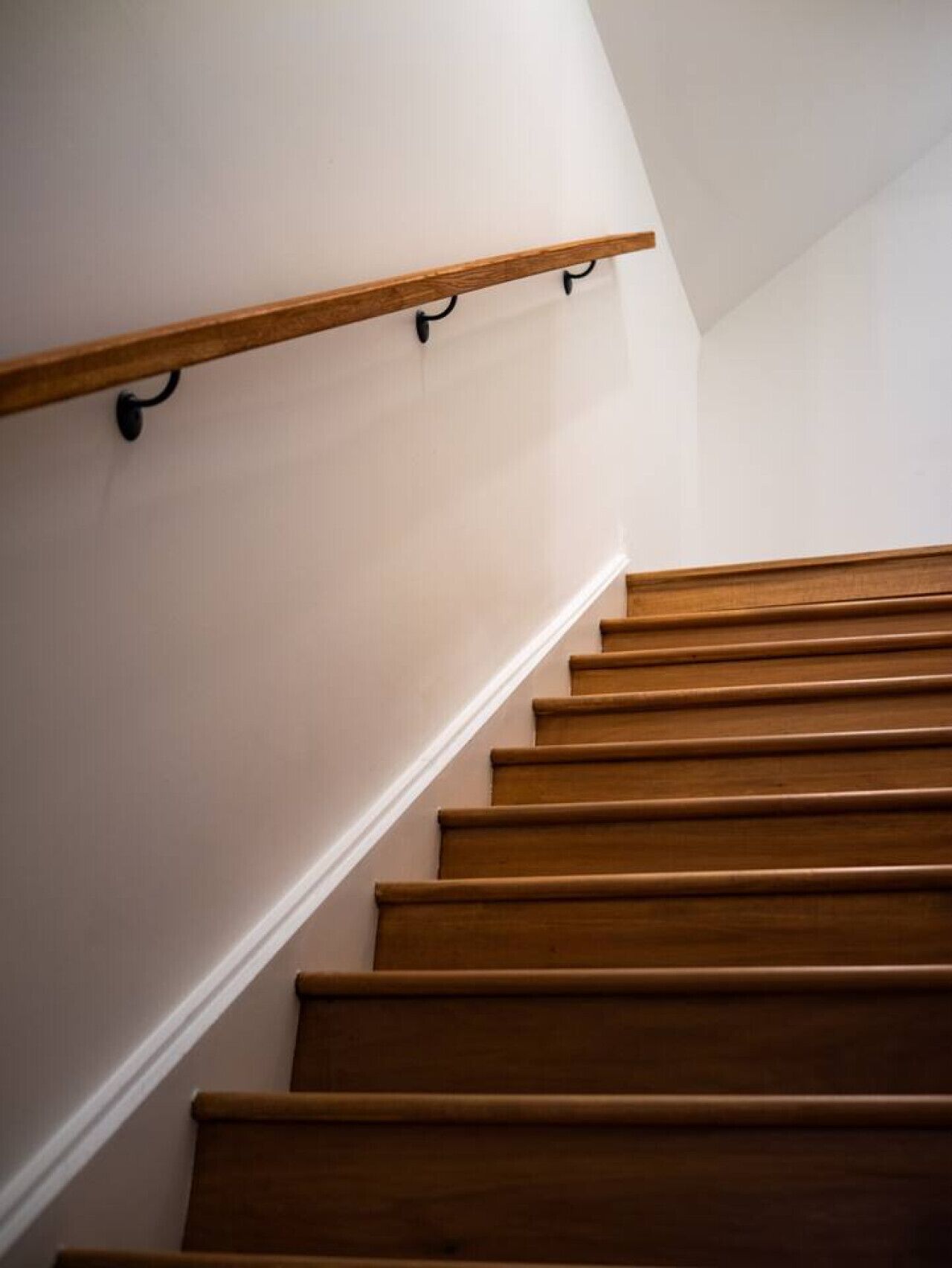 A wooden staircase with a handrail and a white wall.