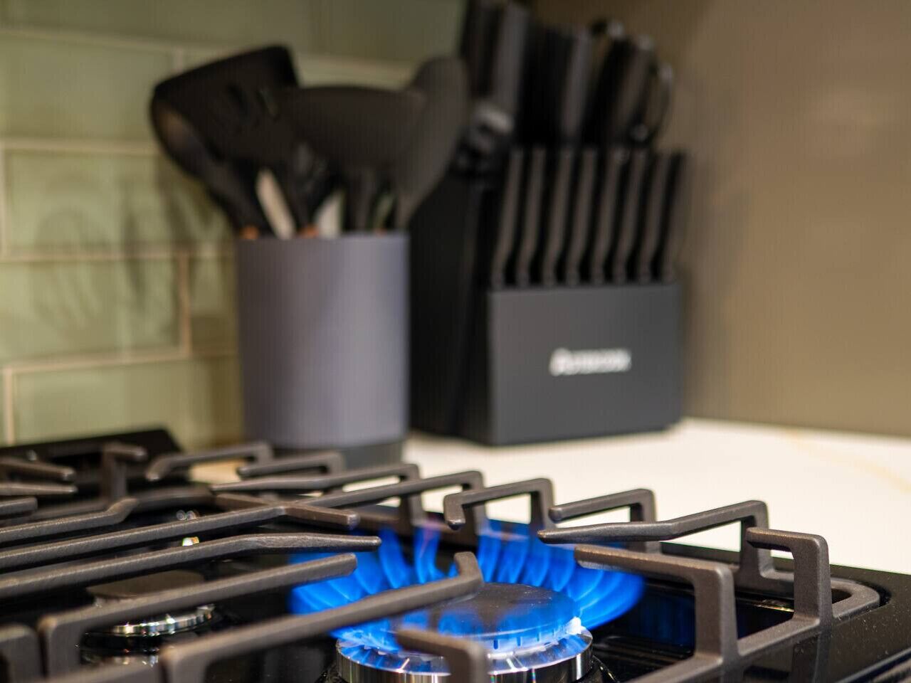 Une cuisine avec une cuisinière à gaz, une flamme bleue et un porte-ustensiles en arrière-plan.