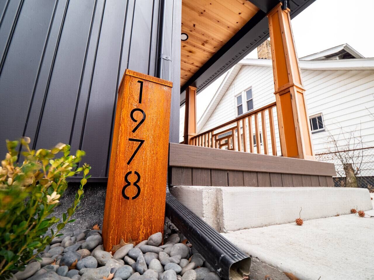 A wooden mailbox with the number 1978, a wooden porch railing, and a concrete step leading to a house.