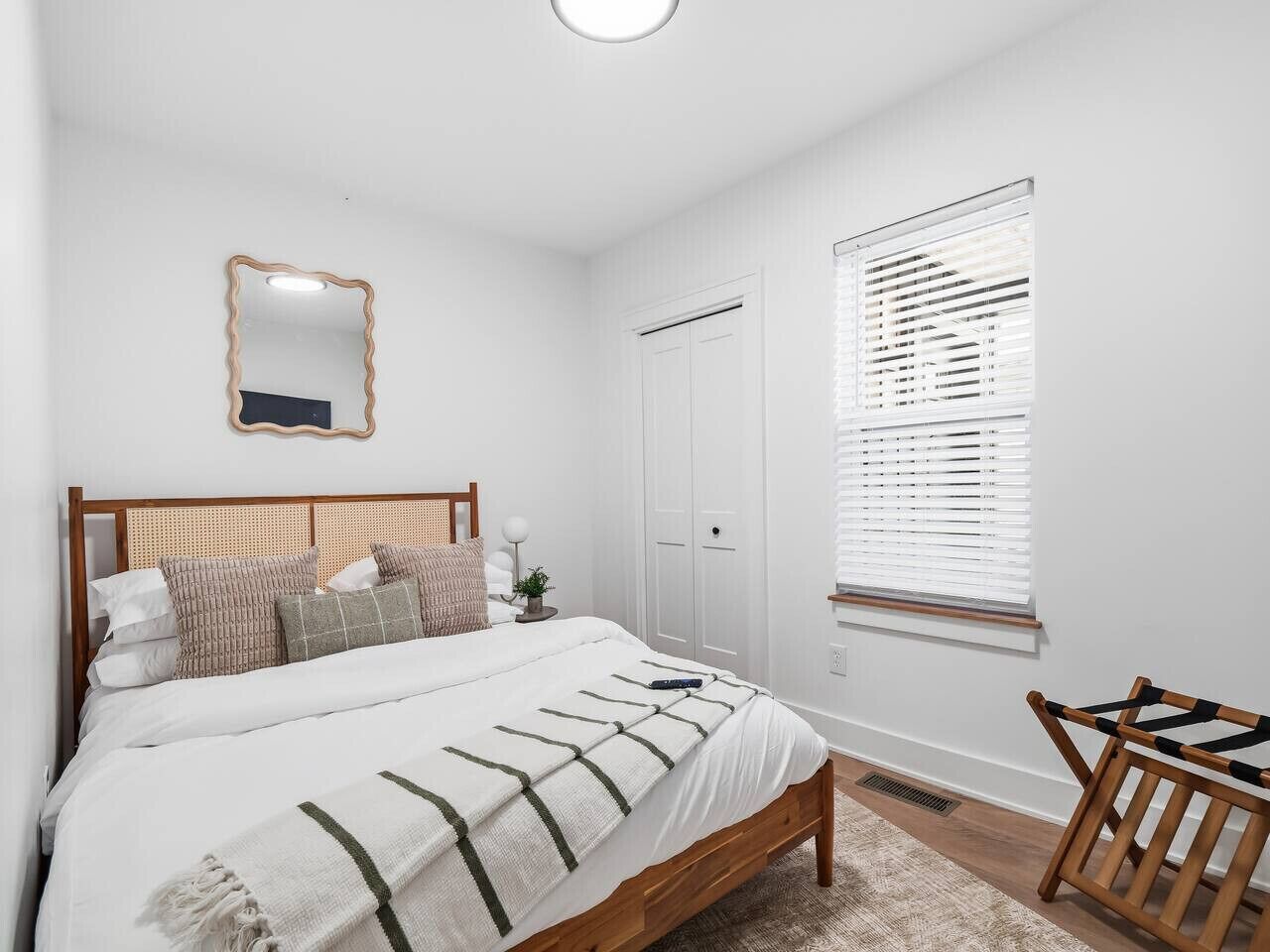 Une chambre à coucher comprenant un lit, une table de chevet, un miroir, une fenêtre avec des stores et une armoire.
