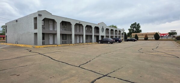 Ein mehrstöckiges Motel mit einer Reihe von Zimmern, einem Parkplatz und einigen parkenden Autos.