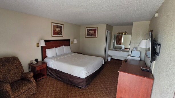 Une chambre d’hôtel avec un lit, une chaise, un bureau, une télévision et un miroir dans la salle de bain.
