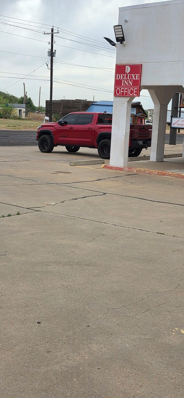 A red SUV parked near a building with a sign reading 'Deluxe Inn Office.' - DELUXE INN SHAMROCK (Shamrock)