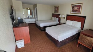 Une chambre d’hôtel avec deux lits, un bureau, une chaise, une lampe, un radiateur et une salle de bain visible au fond.