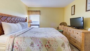 Ein Hotelzimmer mit Bett, Fernseher, einem Korbuschein-Kommode und einem Fenster mit Jalousien.