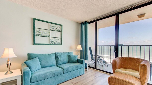 Ein Zimmer mit einer Couch, einem Sessel, einem Tisch und einem großen Fenster mit Blick.