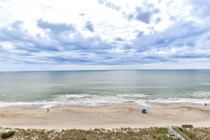 Ein Strand mit sandigem Ufer, wenigen Personen und einem blauen Sonnenschirm.
