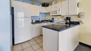 A compact kitchen with white cabinets, a built-in microwave, a coffee maker, and a dishwasher. - Oceanfront 1-bedroom condo in Carolina Beach 0806 (Carolina Beach)