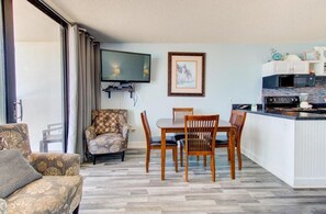 Ein Zimmer mit Esstisch, Stühlen, einer Couch, einem Fernseher und einer Küchenzeile mit Geräten.