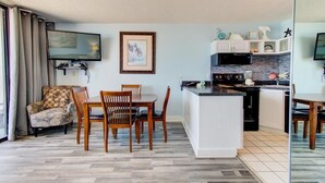 A compact living space with a dining area, kitchenette, and a TV mounted on the wall. - Cozy 1 Bedroom Oceanfront Condo at Carolina Beach 0809 (Carolina Beach)