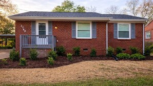 A single-story brick house with a front porch, a small garden, and a clear sky. - Spacious 4BR Family Home with Game Room (Raleigh)