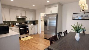 A modern kitchen with white cabinets, stainless steel appliances, and a dining area with a dark wooden table and chairs. - Spacious 4BR Family Home with Game Room (Raleigh)